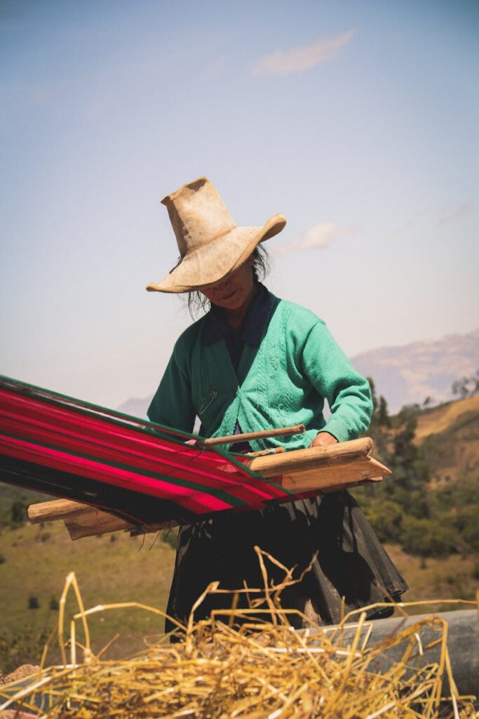 A woman in Cajamarca, Perú, weaving outdoors in traditional attire under a clear sky.